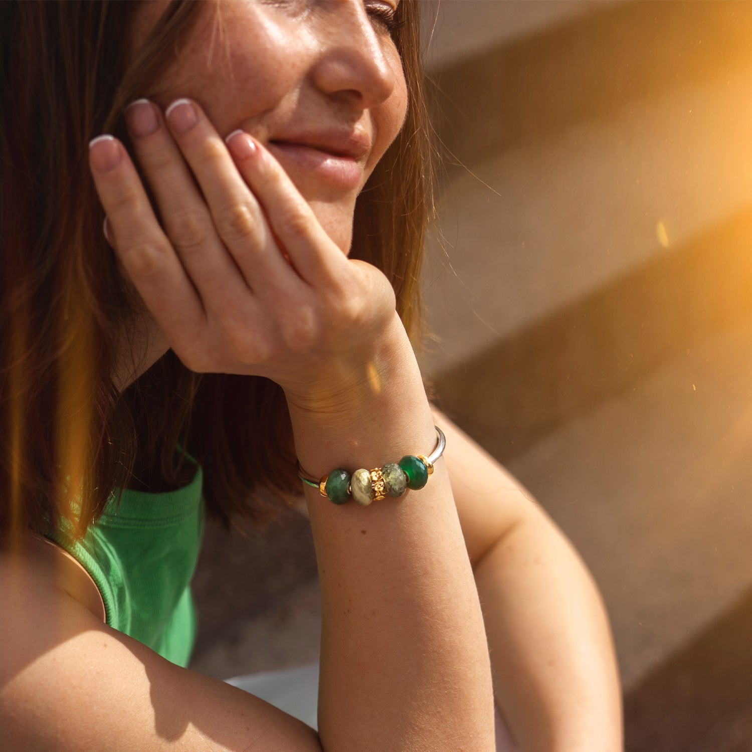 Woman wearing a bracelet with green and gold beads, sunlit background